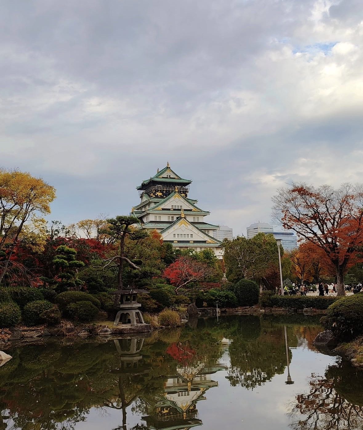 Osaka Castle tower surrounded by cherry blossoms with visitors holding tickets at the entrance gate