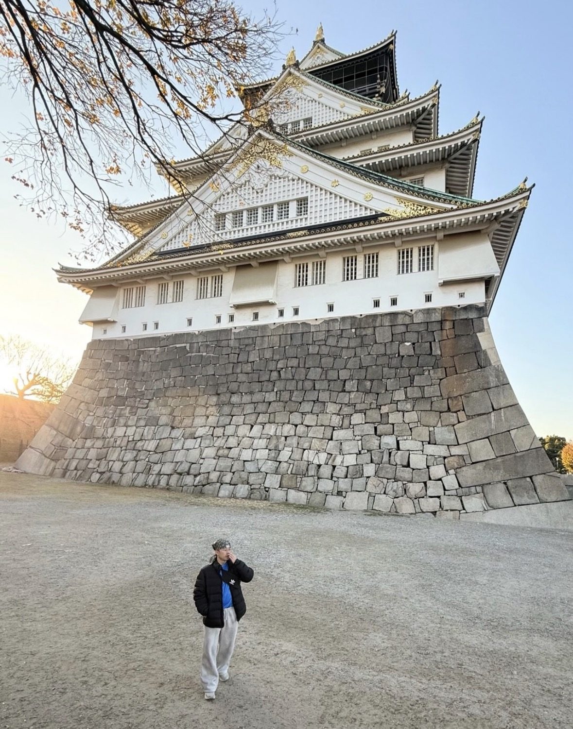 Tourist with backpack and hat walking through Osaka Castle Park gates on a sunny day