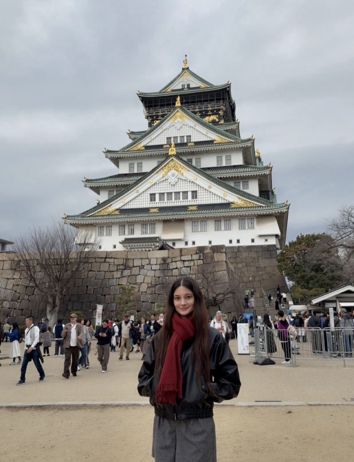 Visitors exploring Osaka Castle grounds with a local guide pointing toward the main tower entrance